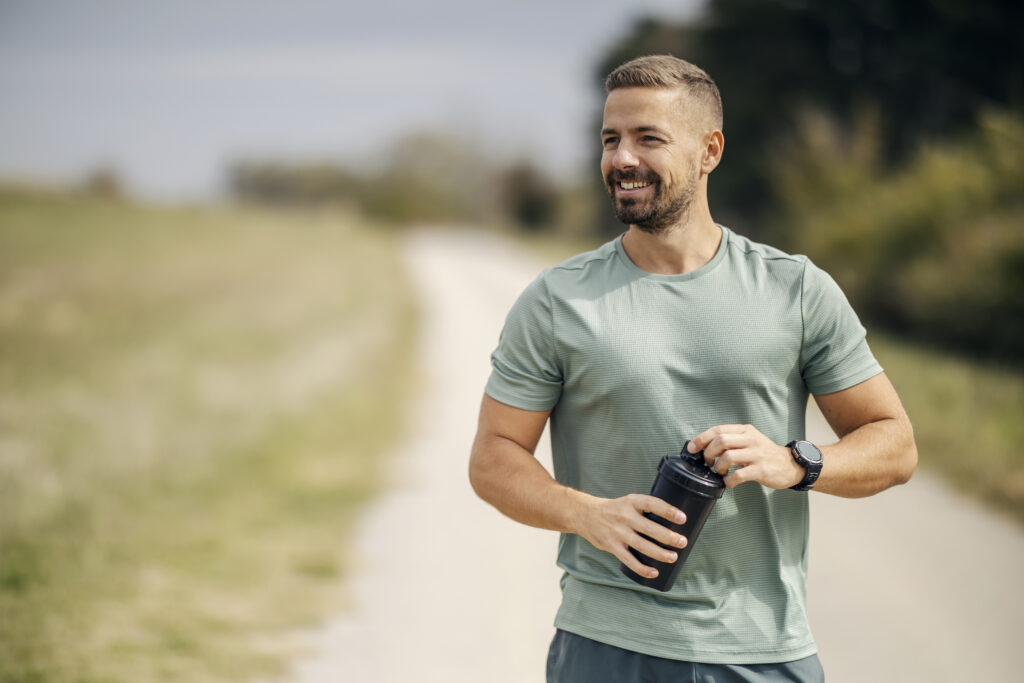 Man smiling holding protein shaker after workout outdoors